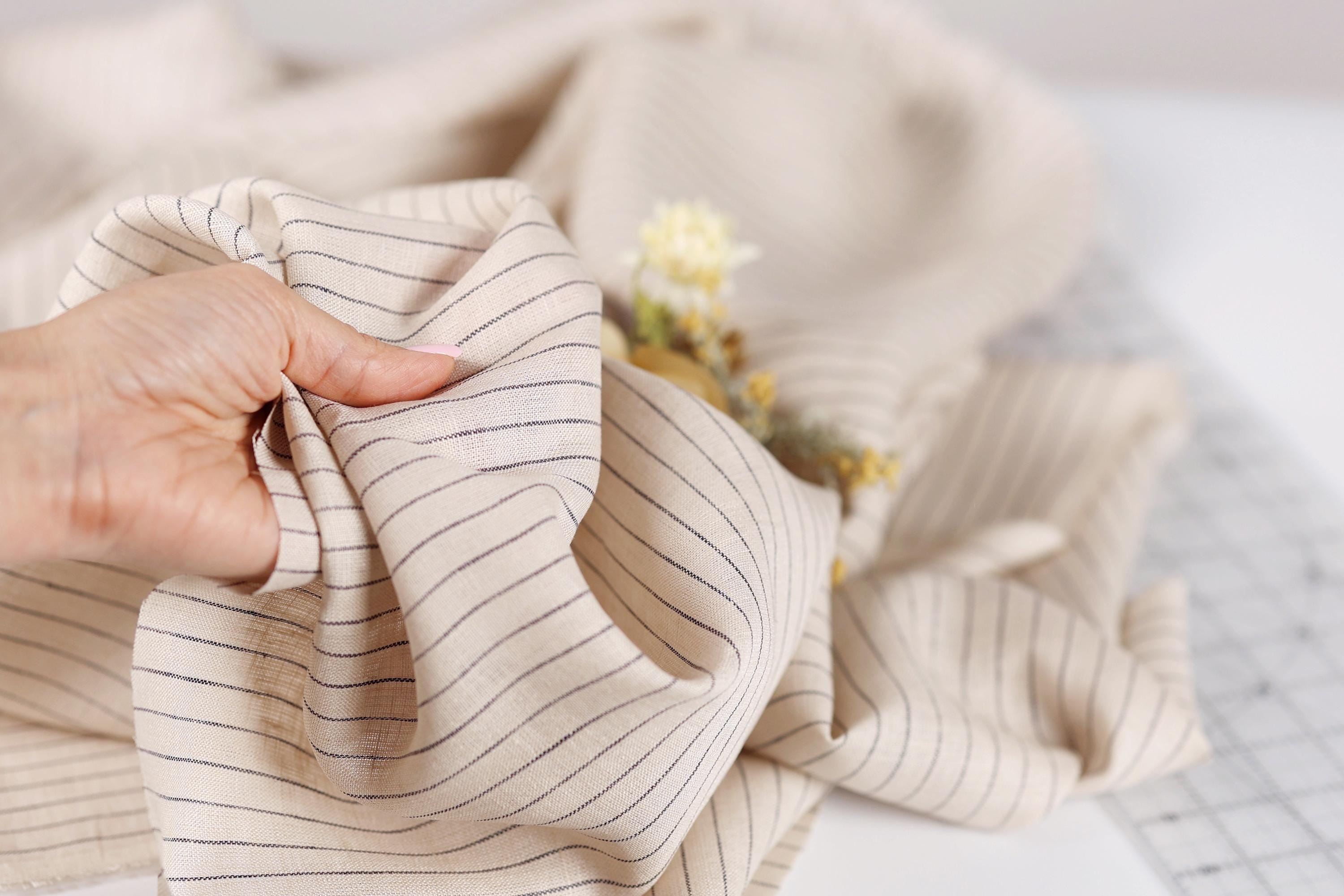 A hand is holding a piece of fabric with black and white striped patterns, with a small flower visible in the background.