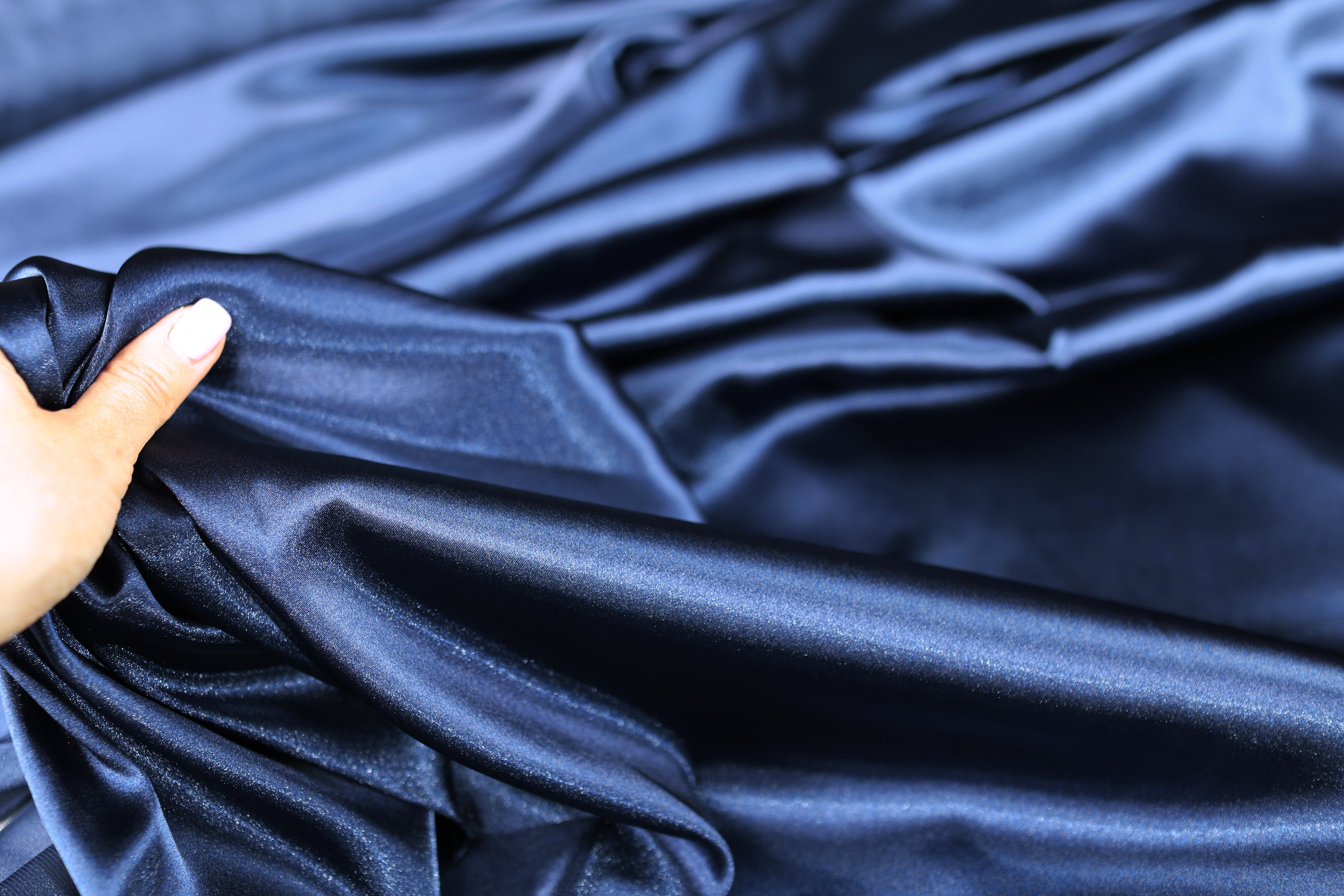 A hand is holding a piece of blue satin fabric, which appears to be shiny and smooth.