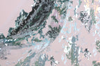 The image is a close-up of a fabric with a metallic, sequined texture. The fabric appears to be a sheer material, with a pattern of green and silver sequins that create a visually striking and intricate design. The fabric is not a single piece but rather a part of a larger fabric, as suggested by the background that is a light pink color. The image does not contain any discernible text or countable objects, and the focus is on the detailed and textured appearance of the fabric.