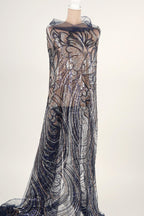 A mannequin wearing a long, flowing dress with a sheer, sequined bodice and a sheer, black and silver patterned skirt.