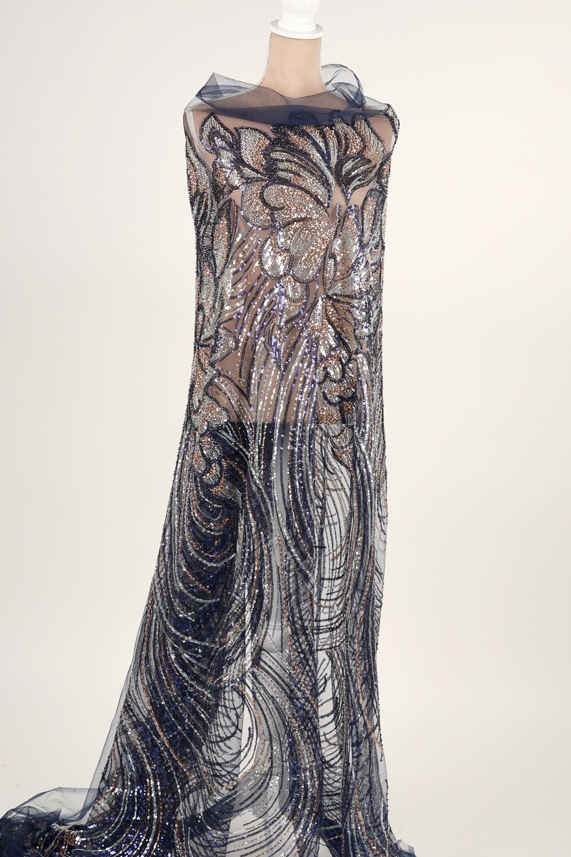 A mannequin wearing a long, flowing dress with a sheer, sequined bodice and a sheer, black and silver patterned skirt.