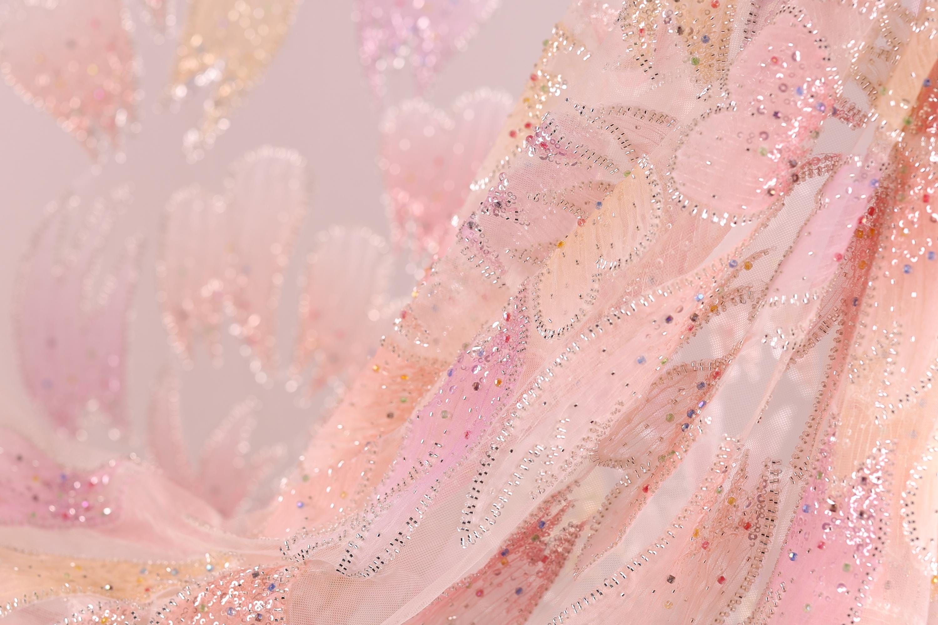 a close-up view of a delicate, pink and white fabric with a floral pattern. The fabric appears to be made of sheer material, giving it a soft and delicate appearance. The background is blurred, drawing focus to the fabric and its intricate details.
