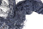 a close-up view of a fabric with a dark blue, glittery, and sequined pattern. The fabric appears to be a type of lace or sheer material, with a textured and shiny appearance.