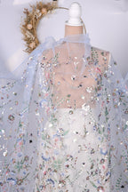 a close-up view of a delicate, intricately embroidered dress with a floral pattern. The dress appears to be made of sheer fabric, giving it a delicate and ethereal appearance. The floral design is visible on the fabric, adding a touch of elegance and sophistication to the garment.