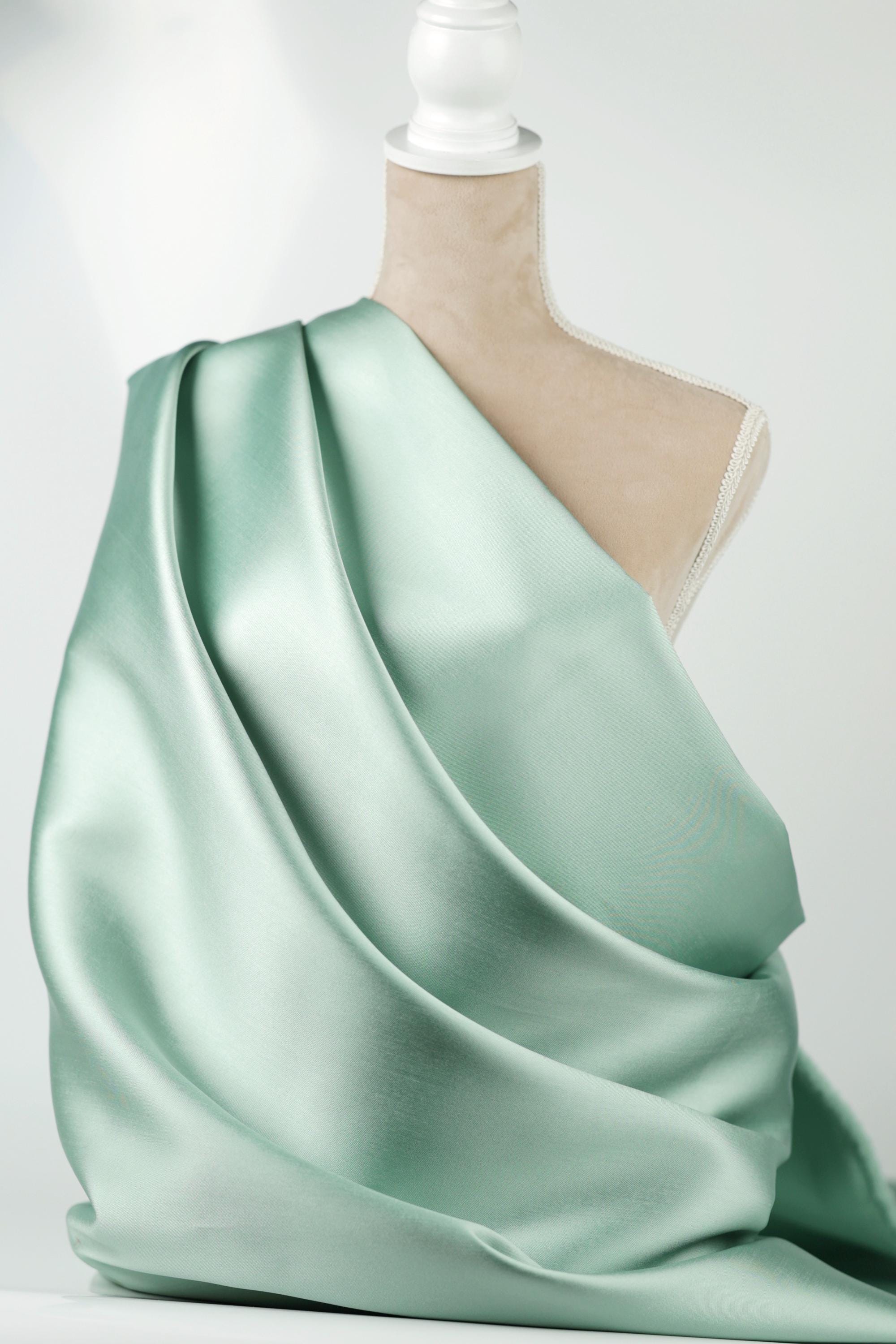 A mannequin wearing a flowing, mint green satin fabric draped over its body.