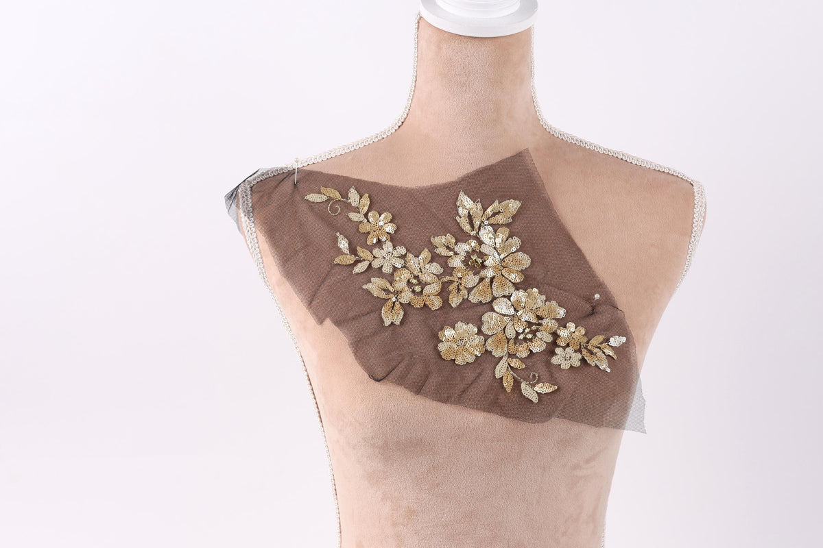 A mannequin with a brown fabric piece on its chest, featuring a floral design with gold and white flowers.