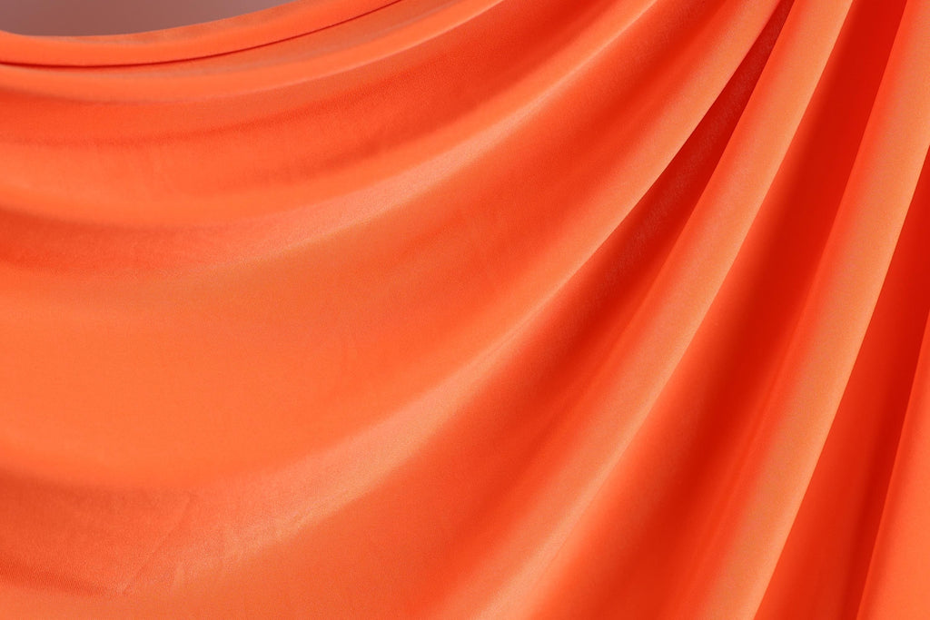 The image is a close-up of a bright orange fabric, possibly a sheer or sheer-like material, with a smooth and flowing texture.