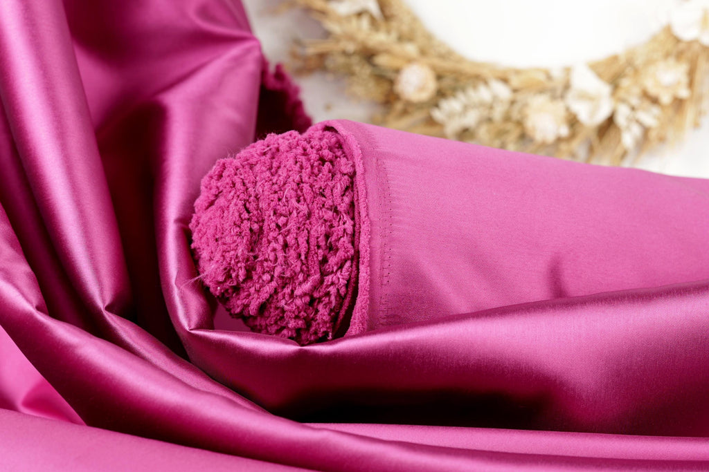 A close-up view of a vibrant pink fabric, possibly silk or satin, with a fluffy, textured appearance. The fabric is folded and draped, creating a visually appealing and luxurious scene.