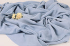 a close-up view of a crumpled light blue fabric with a single yellow flower resting on top of it.