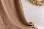 a close-up view of a brown fabric, possibly a piece of clothing or a textile, with a blurred background that includes a wreath made of dried flowers.