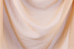 The image is a close-up of a soft, flowing fabric, possibly a sheer or sheer-like material, with a light peach or pale yellow color. The fabric appears to be made of a delicate, sheer material, which gives it a delicate and airy appearance.
