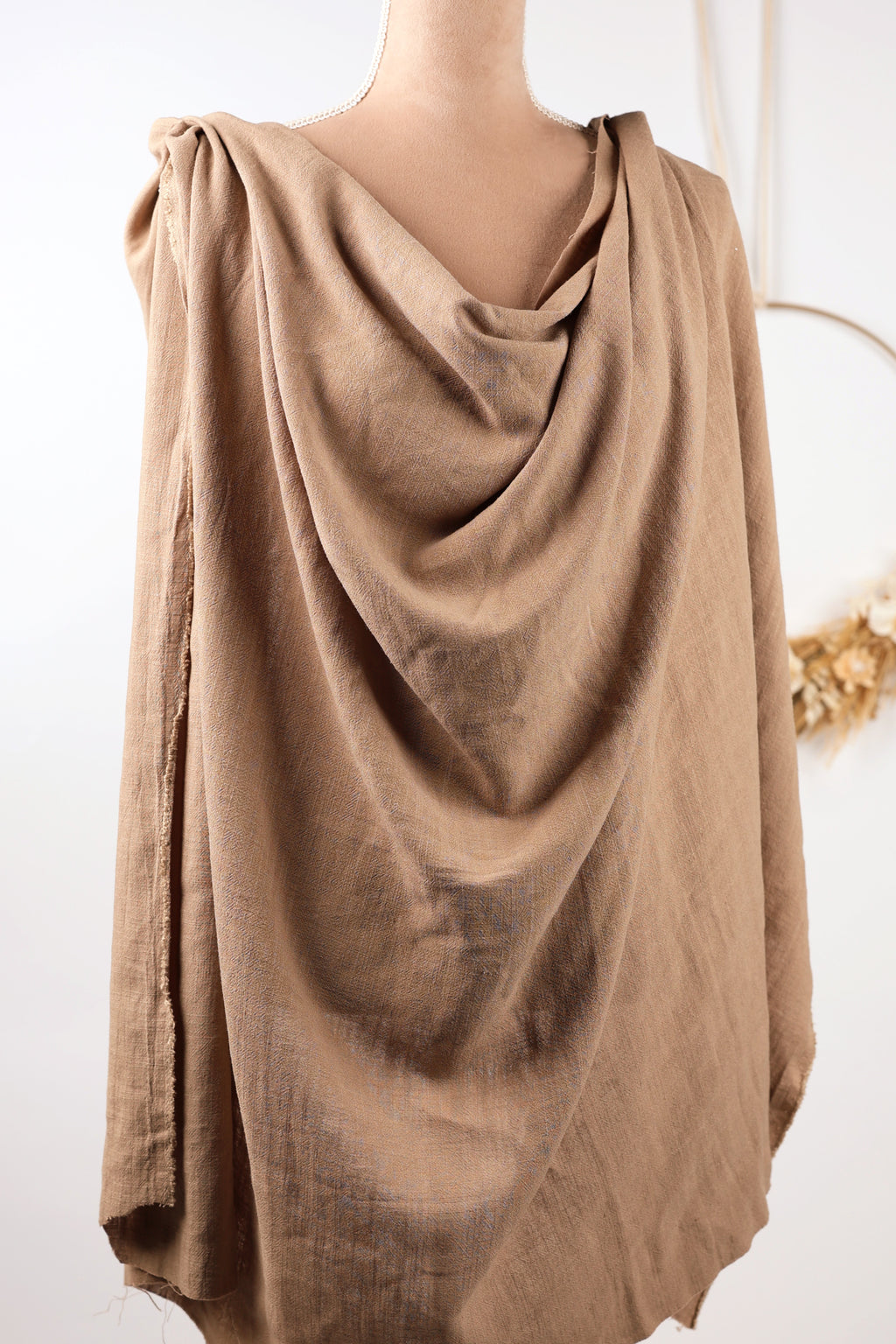A mannequin wearing a beige, draped garment with a flowing, draped appearance.