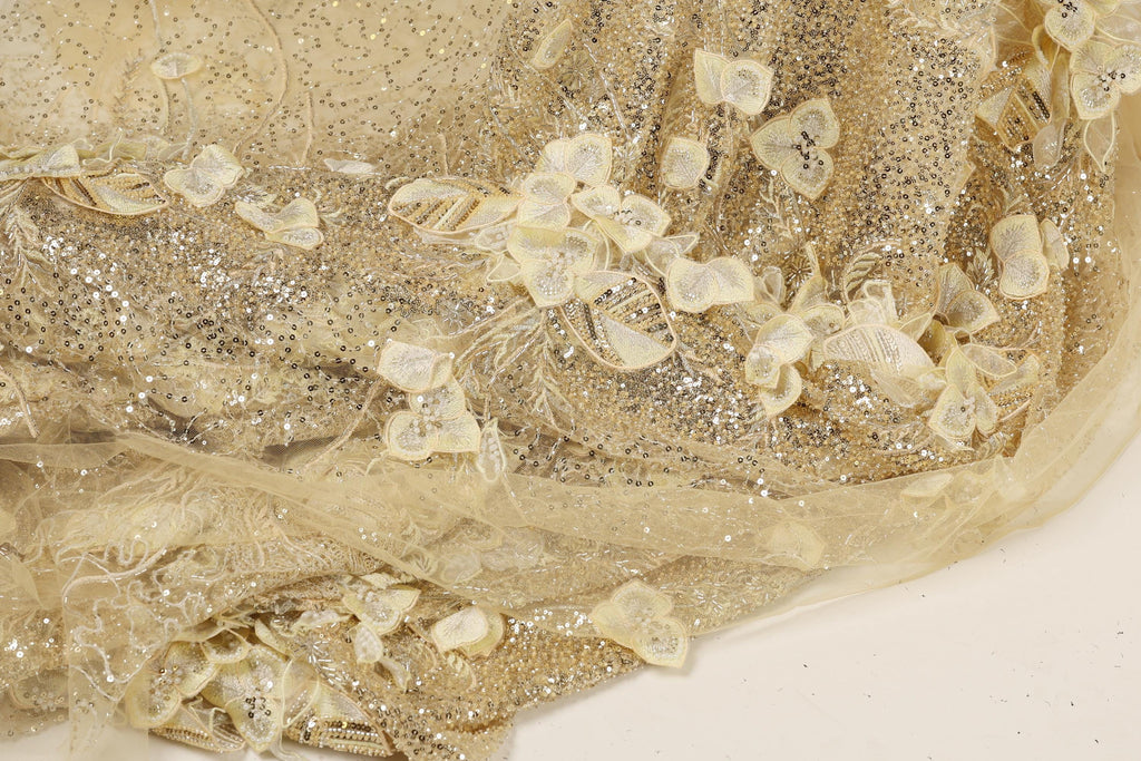 The image is a close-up of a fabric with a gold and white color scheme, featuring a pattern of small white flowers or leaves scattered throughout the fabric.