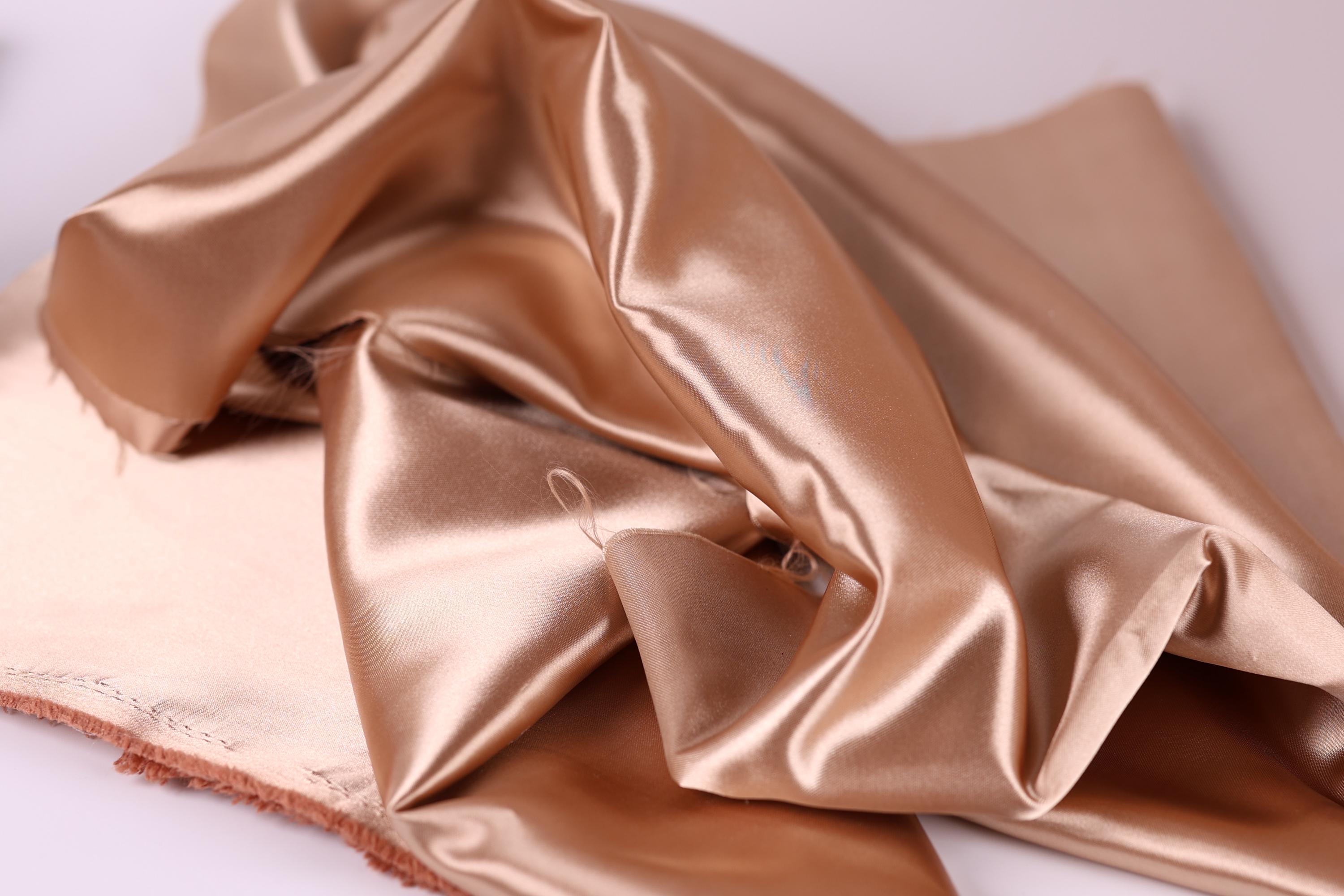 A close-up image of a crumpled, shiny fabric with a golden-brown color.
