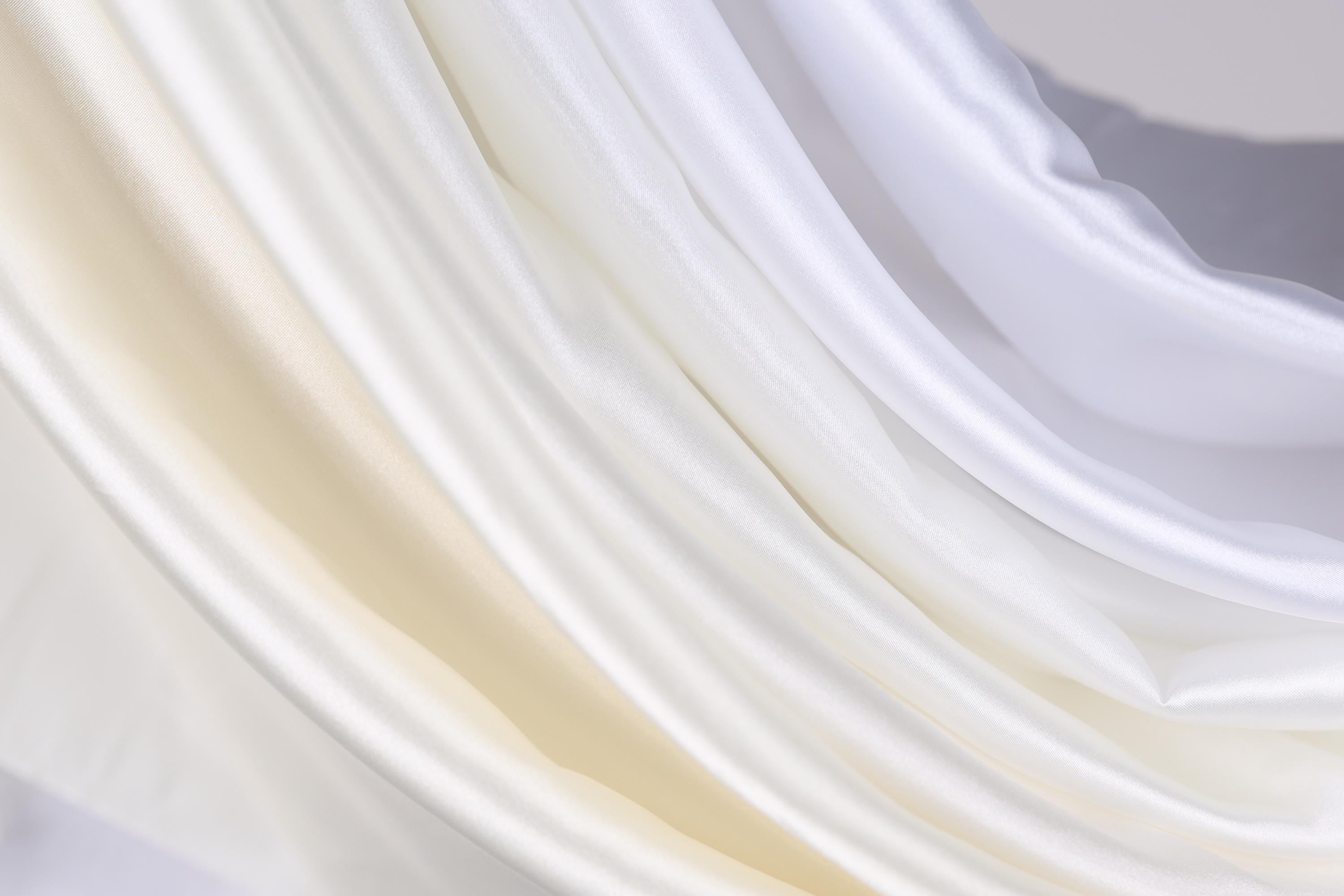 The image is a close-up of a fabric with a soft, flowing texture in shades of white and beige.