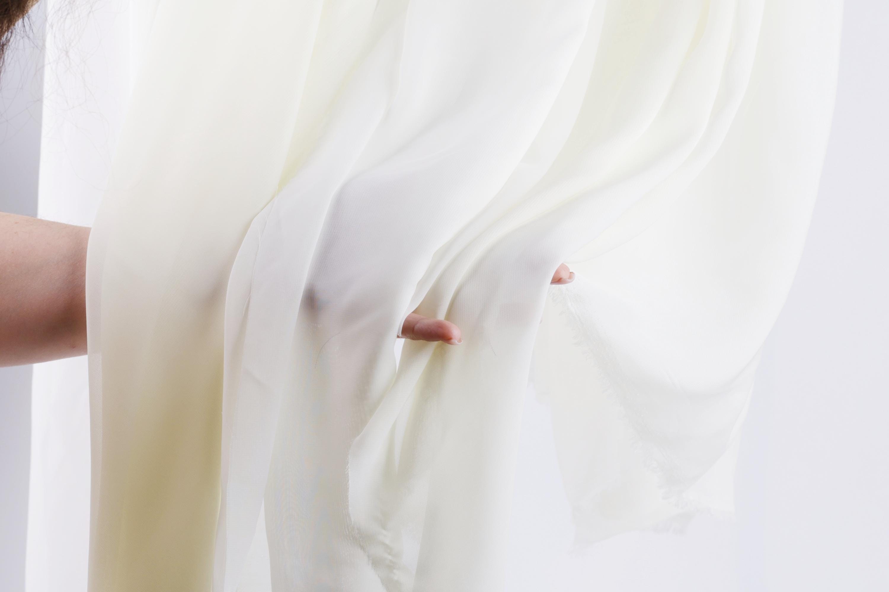 A hand is holding a white fabric, possibly a curtain or a sheet, with the fabric partially pulled back.