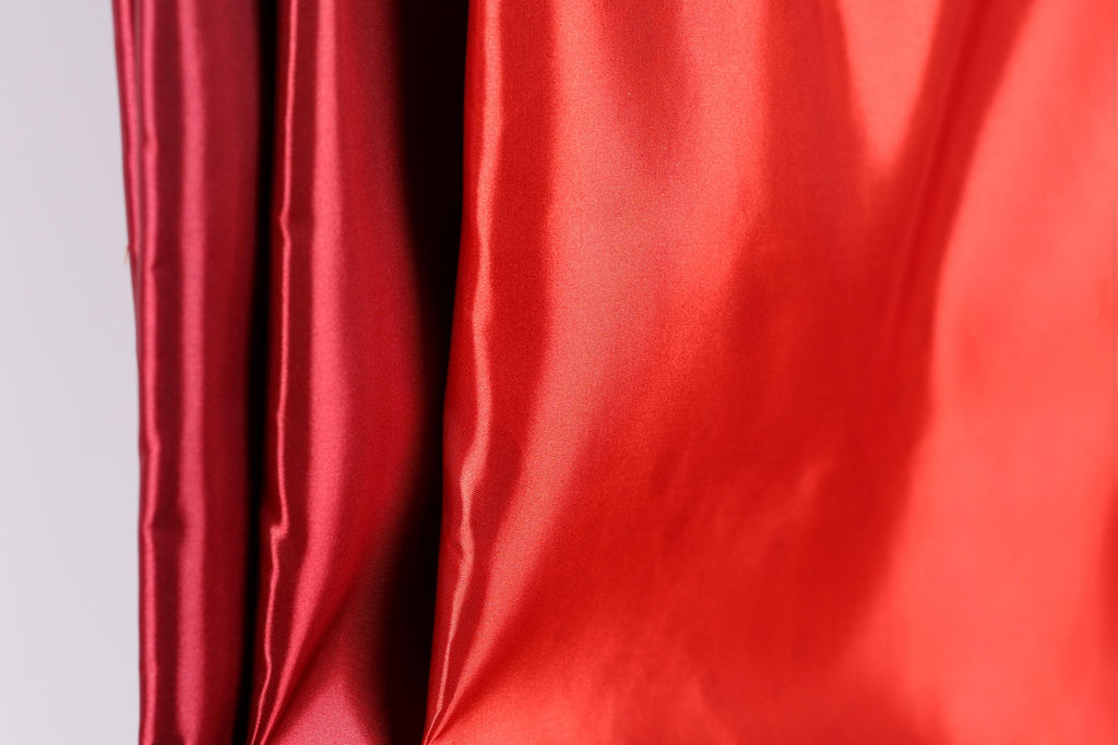 a close-up view of a red fabric, with a blurred red fabric visible in the background.