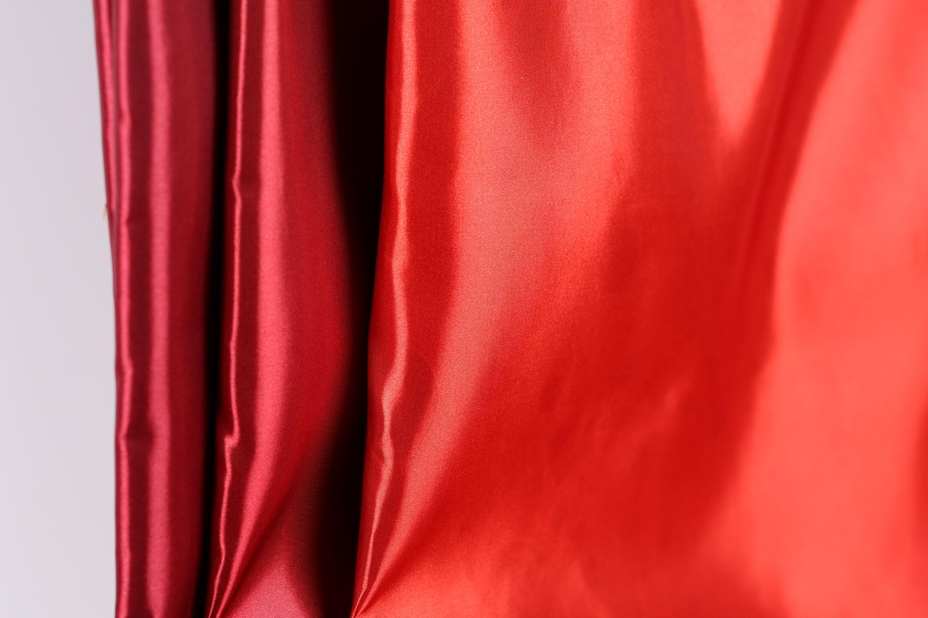 a close-up view of a red fabric, with a blurred red fabric visible in the background.
