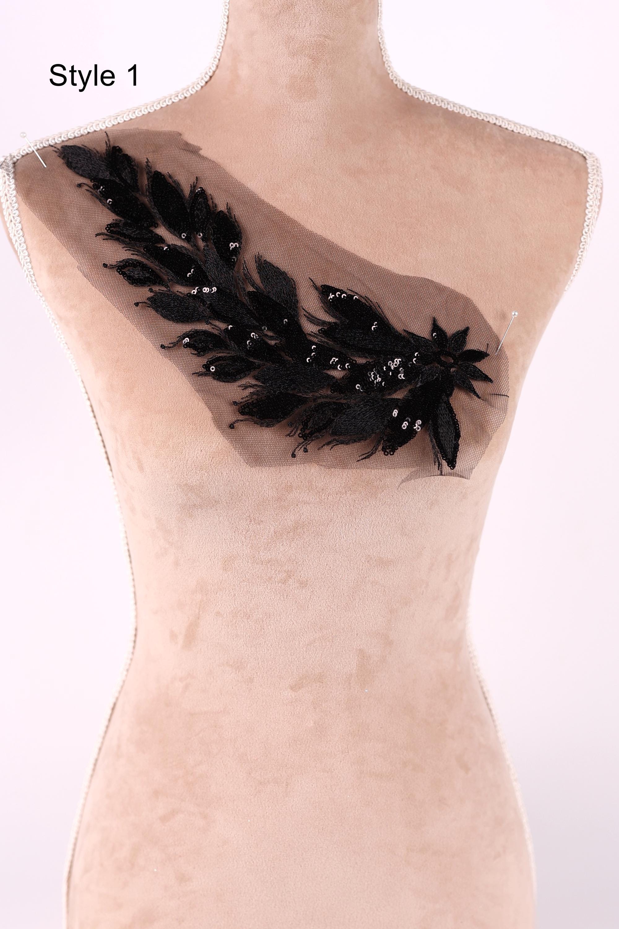 A mannequin with a decorative black feather embellishment on its shoulder.