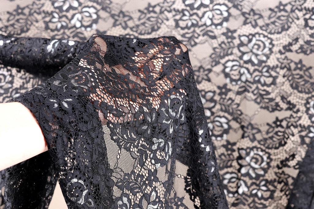 A close-up view of a hand holding a piece of black lace fabric with a floral pattern.