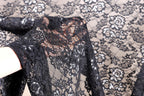 A close-up view of a hand holding a piece of black lace fabric with a floral pattern.