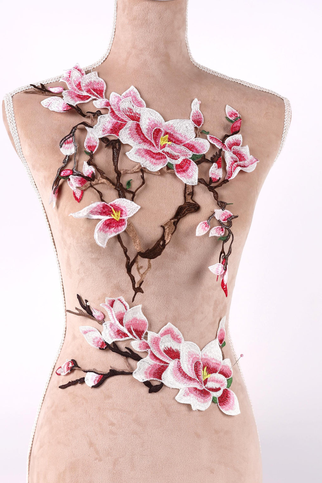 A mannequin torso with a floral embroidered design on it, featuring pink and white flowers and branches.