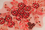 a close-up view of a delicate, intricate floral embroidery with red and black sequins. The embroidery is composed of numerous small flowers and leaves, creating a visually striking and detailed design.