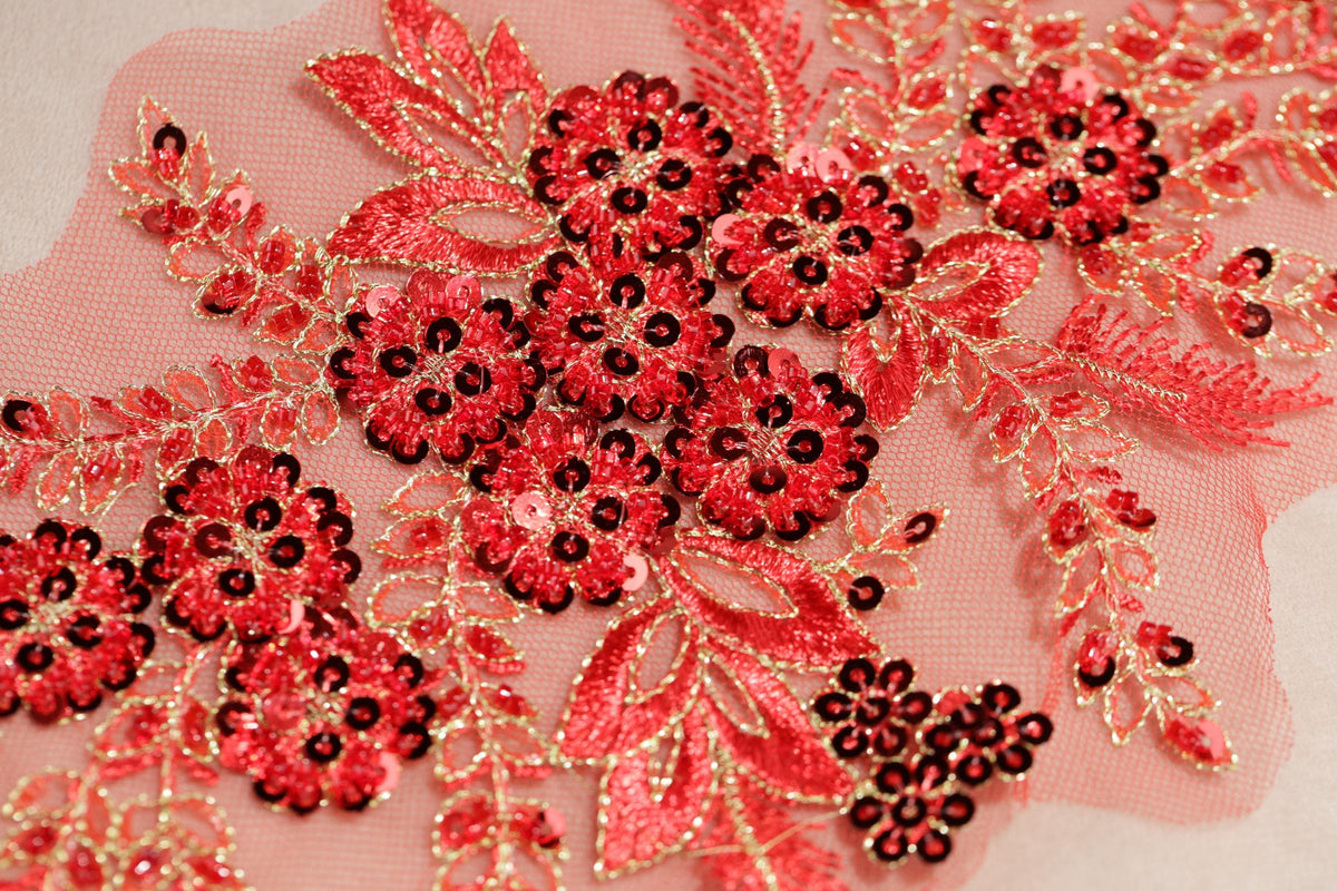 a close-up view of a delicate, intricate floral embroidery with red and black sequins. The embroidery is composed of numerous small flowers and leaves, creating a visually striking and detailed design.