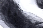 a close-up view of a black, shiny, and glittery fabric, possibly a sheer or sheer-like material. The fabric appears to be made of a sheer or sheer-like material, which is characterized by its transparent or translucent nature, allowing light to pass through it. The fabric has a shiny, glittery texture that adds a touch of sparkle and elegance to the image.
