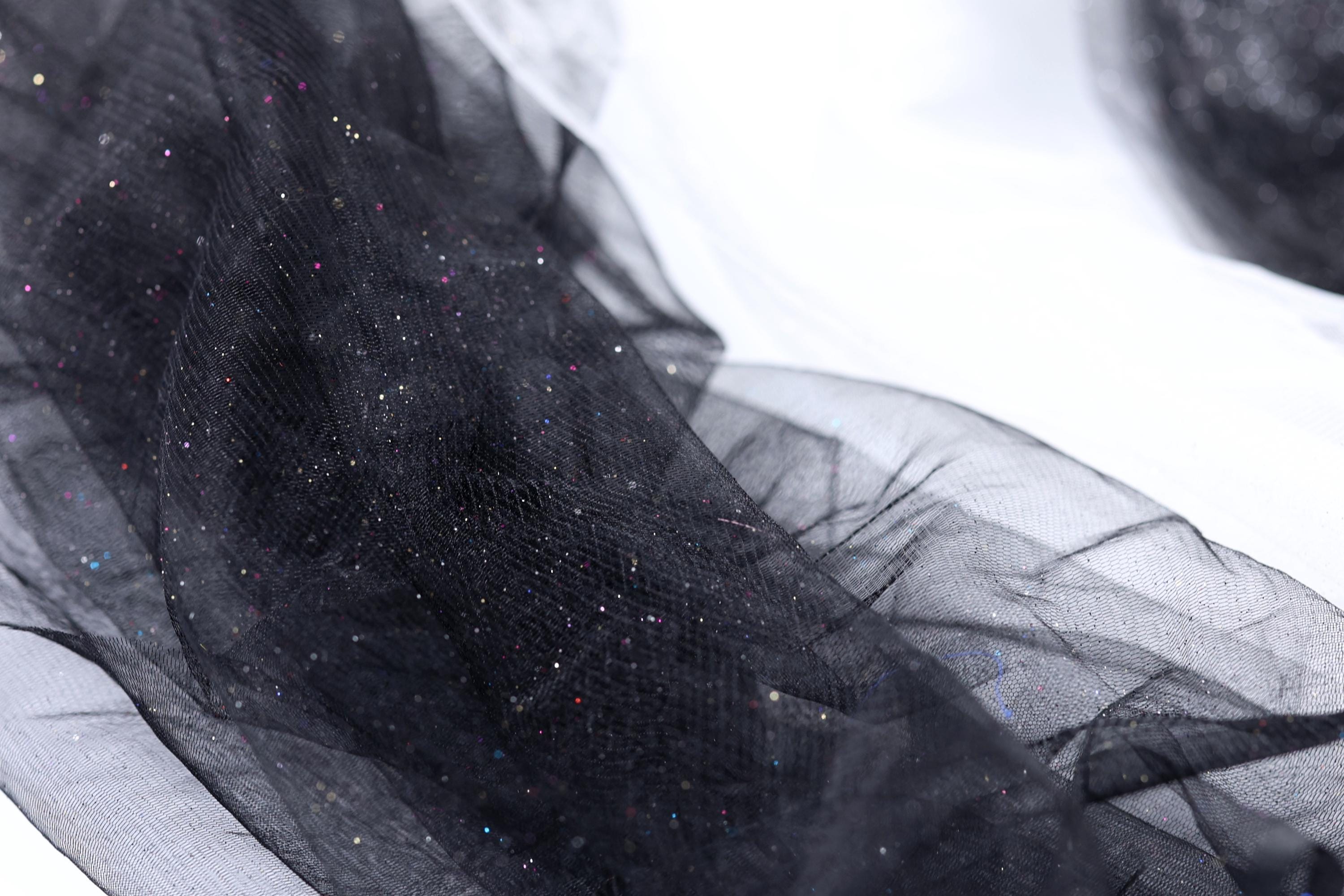 a close-up view of a black, shiny, and glittery fabric, possibly a sheer or sheer-like material. The fabric appears to be made of a sheer or sheer-like material, which is characterized by its transparent or translucent nature, allowing light to pass through it. The fabric has a shiny, glittery texture that adds a touch of sparkle and elegance to the image.
