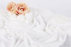 two pink roses resting on a white, crumpled fabric.