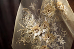 a close-up view of a delicate, intricately embroidered fabric with a floral design. The fabric appears to be a sheer material, with gold-colored flowers and leaves adorning the surface. The embroidery is detailed and appears to be handcrafted, showcasing the skill and artistry involved in creating this piece of textile art.