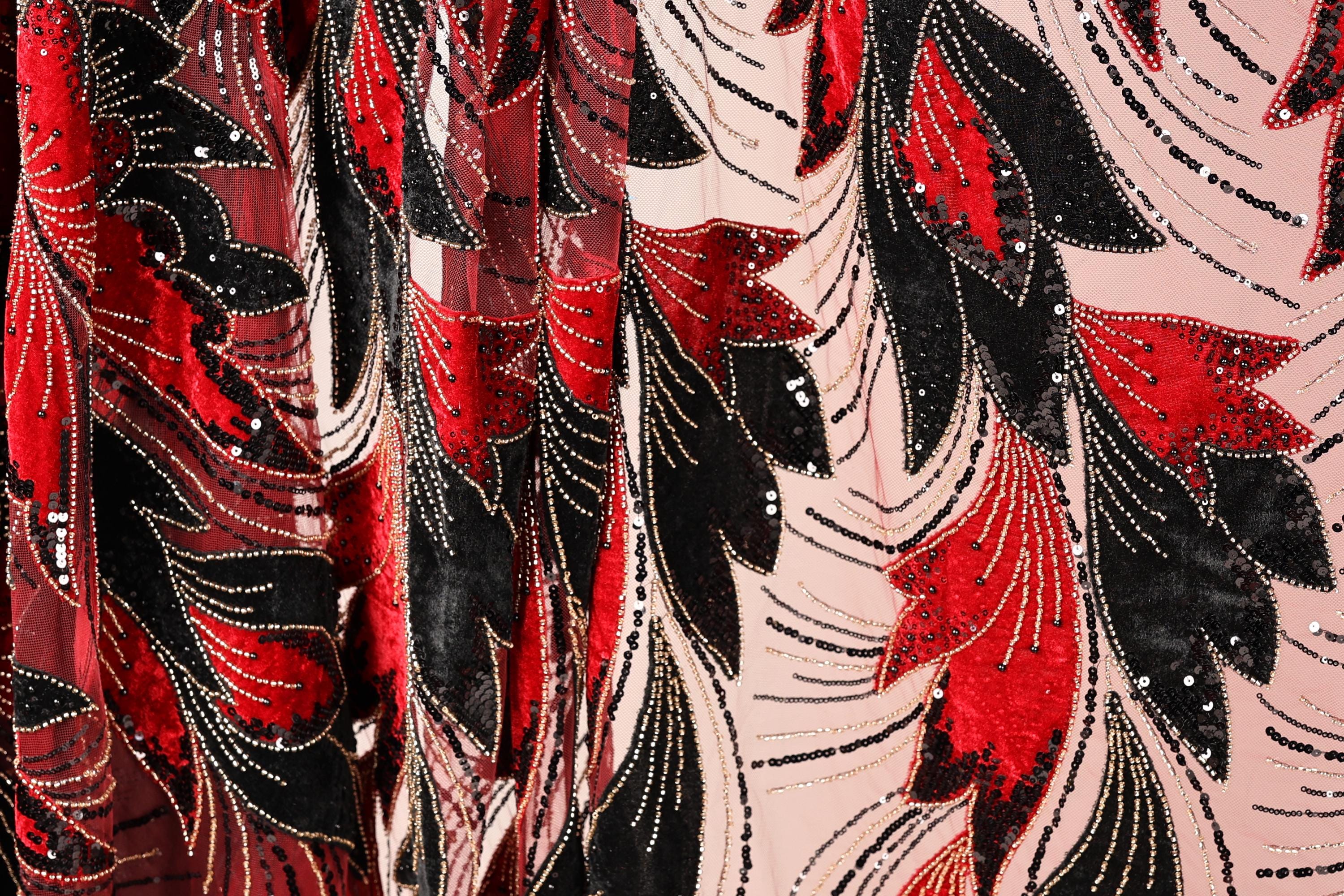 a close-up view of a fabric with a striking pattern of red, black, and white sequins and beads. The pattern is intricate and detailed, with the sequins and beads creating a visually captivating design. The fabric appears to be a sheer material, which adds to the overall aesthetic of the image.
