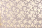a close-up view of a fabric with a floral pattern. The fabric appears to be made of a light-colored material, possibly lace or a similar type of material. The pattern consists of numerous small white flowers or leaves scattered across the fabric, creating a visually appealing and intricate design.