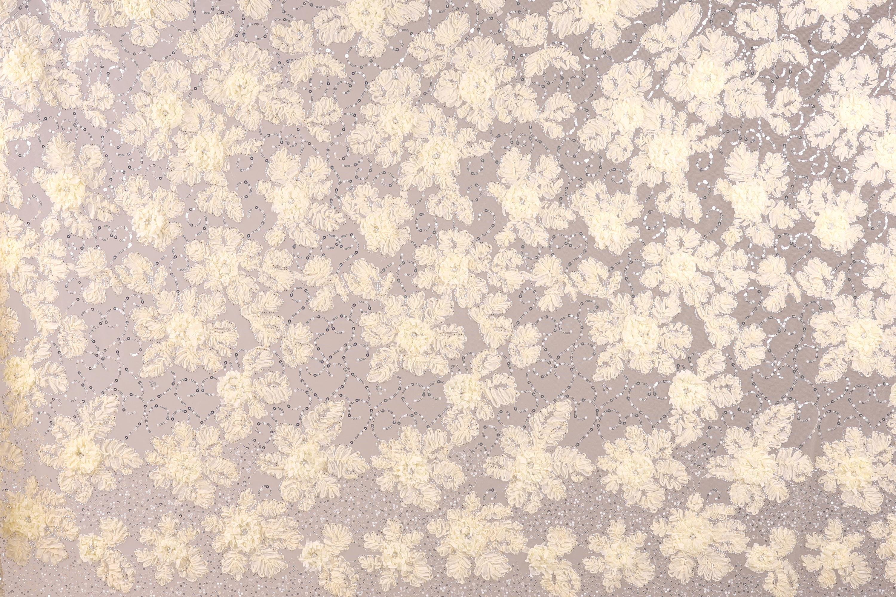 a close-up view of a fabric with a floral pattern. The fabric appears to be made of a light-colored material, possibly lace or a similar type of material. The pattern consists of numerous small white flowers or leaves scattered across the fabric, creating a visually appealing and intricate design.