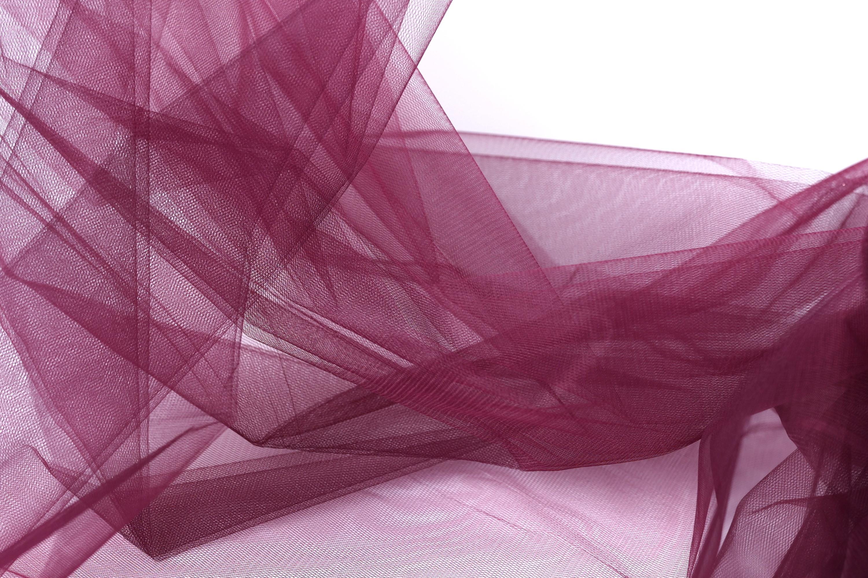 The image is a close-up of a fabric with a maroon or burgundy color, featuring a textured and layered appearance.