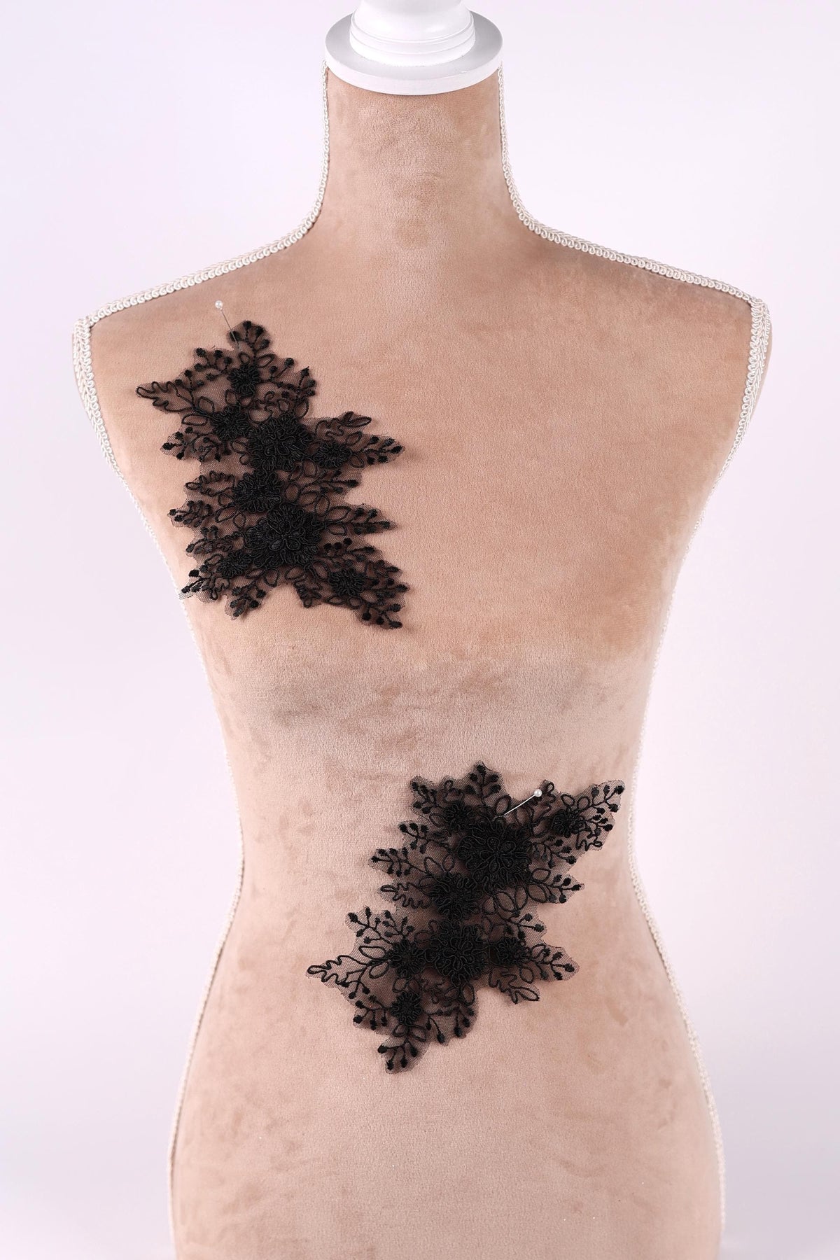 A mannequin with a beige body and black lace appliques on its torso.