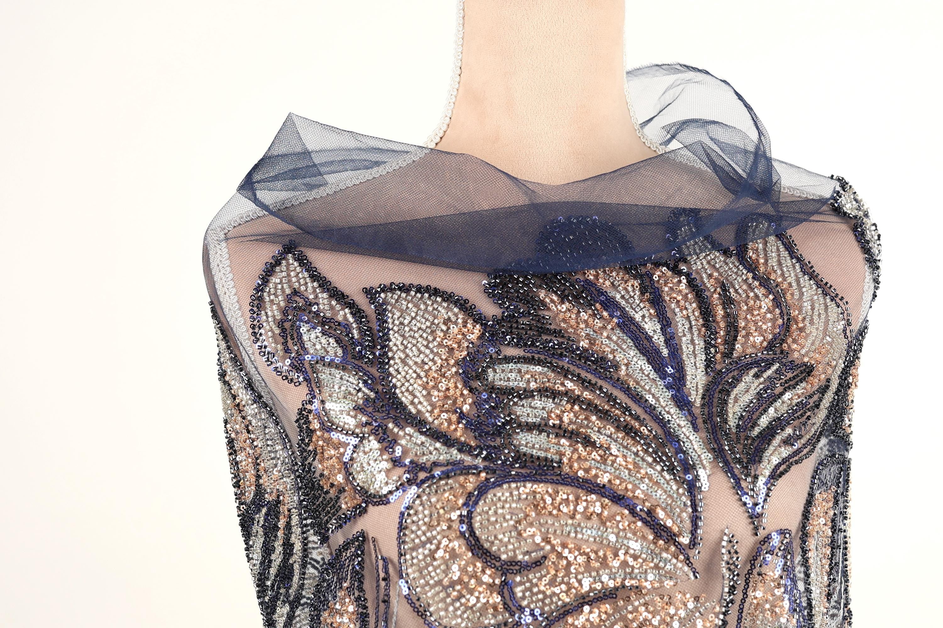 A mannequin wearing a dress with a sheer, sequined bodice and a blue, sheer, floral-patterned collar.