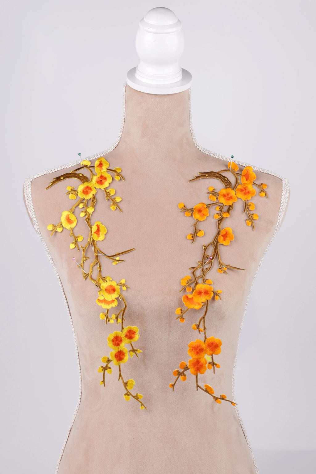 A mannequin with a beige body and floral embroidery on its shoulders. The embroidery consists of yellow and orange flowers with green leaves, creating a vibrant and eye-catching design.