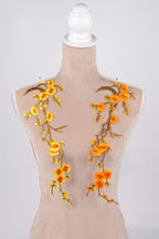 A mannequin with a beige body and floral embroidery on its shoulders. The embroidery consists of yellow and orange flowers with green leaves, creating a vibrant and eye-catching design.