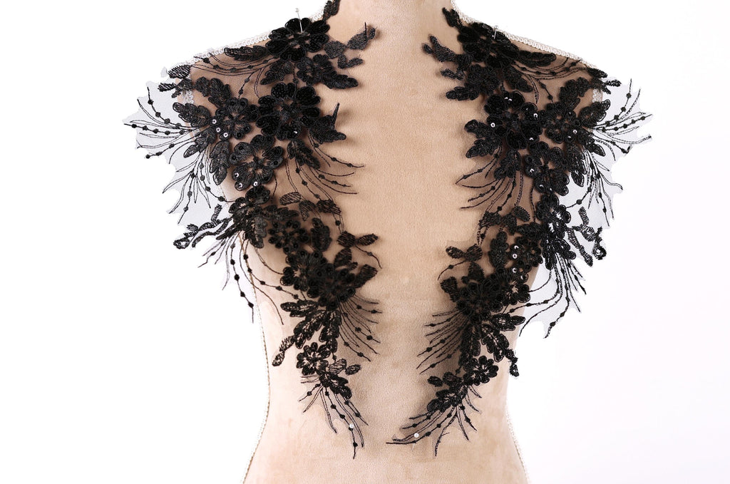 A mannequin wearing a black lace dress with intricate floral patterns.