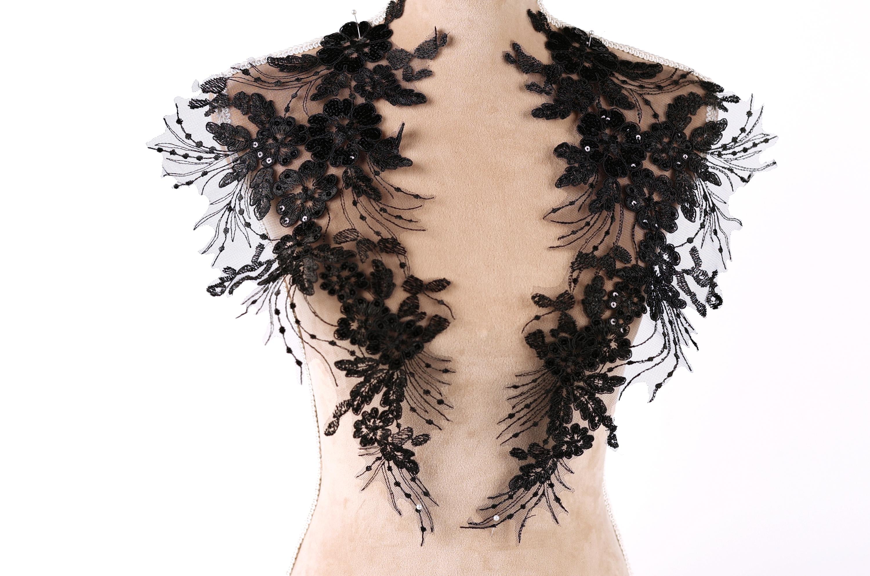 A mannequin wearing a black lace dress with intricate floral patterns.