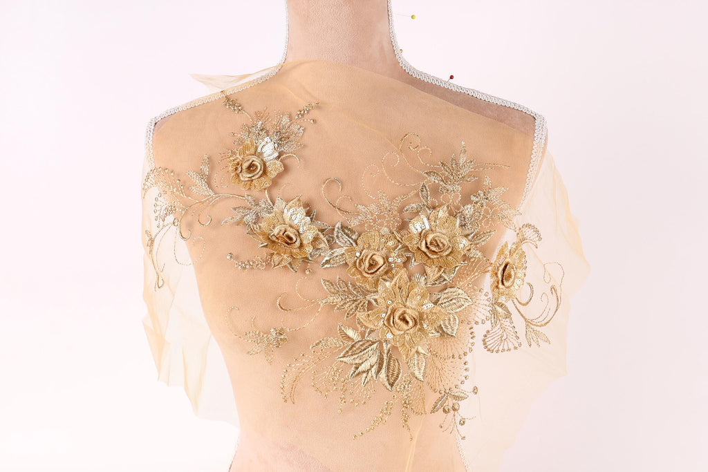 A mannequin with a sheer, golden-colored fabric draped over its back, adorned with intricate floral embroidery.