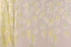 a close-up view of a fabric with a floral pattern, including yellow and white flowers and leaves. The fabric appears to be made of a shiny, glittery material, giving it a sparkly and delicate appearance.