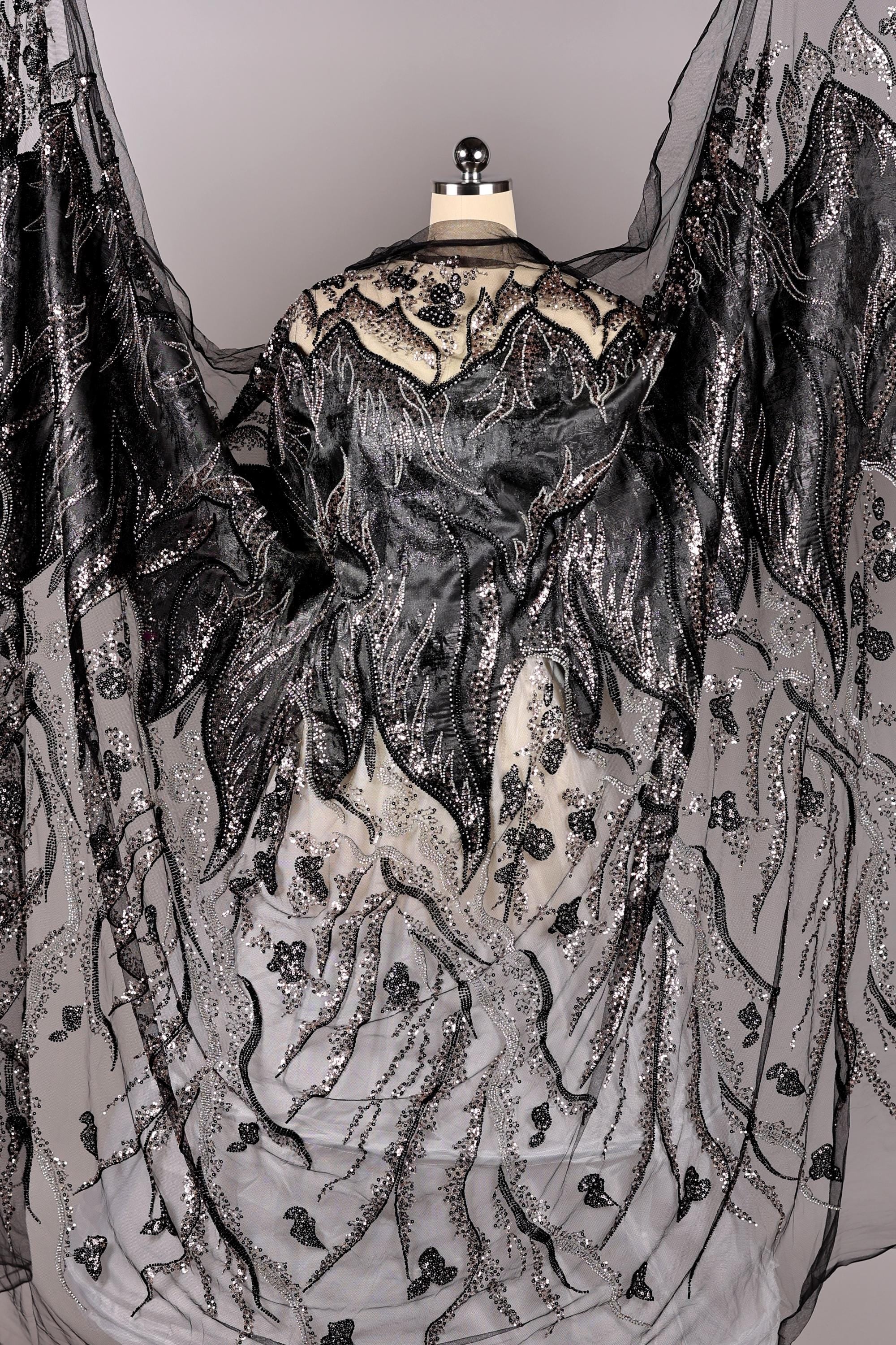 a black and white dress with intricate, shimmering embroidery and a flowing, draped cape-like garment.
