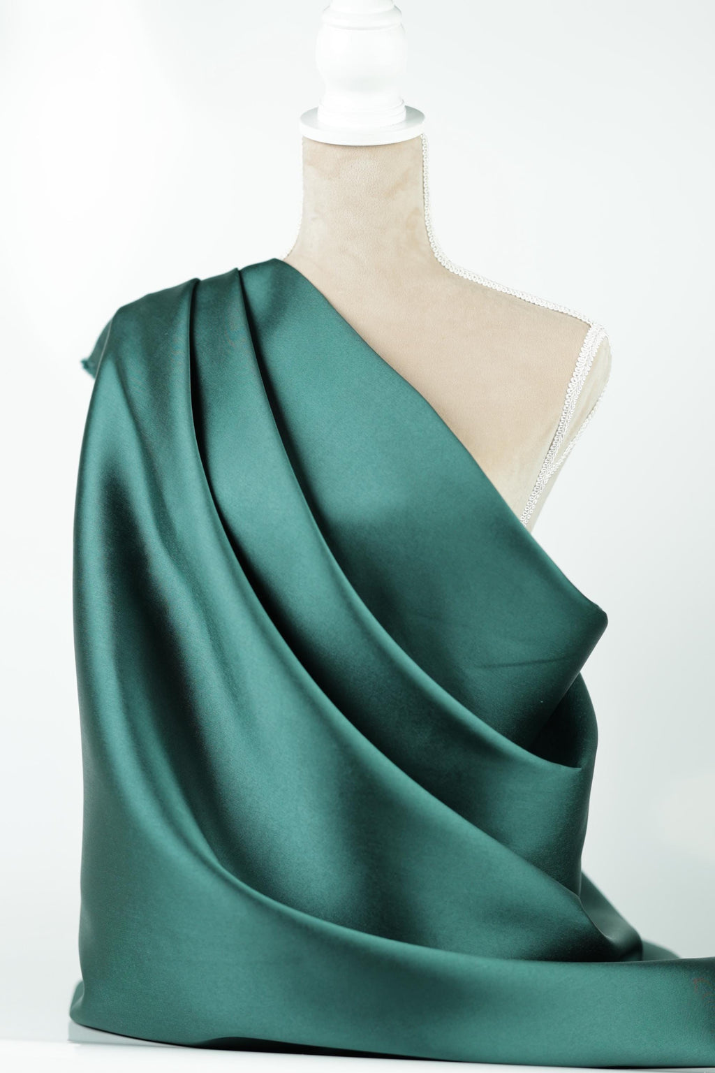 A close-up view of a green satin fabric draped over a mannequin, with a beige fabric piece attached to the mannequin's neck.