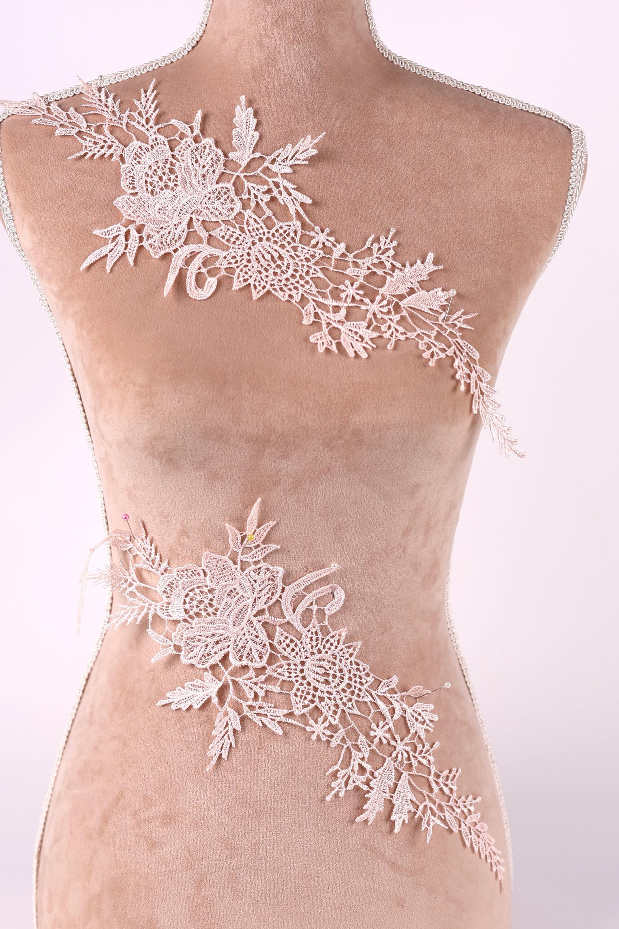 A mannequin torso with delicate white lace floral embroidery on it.