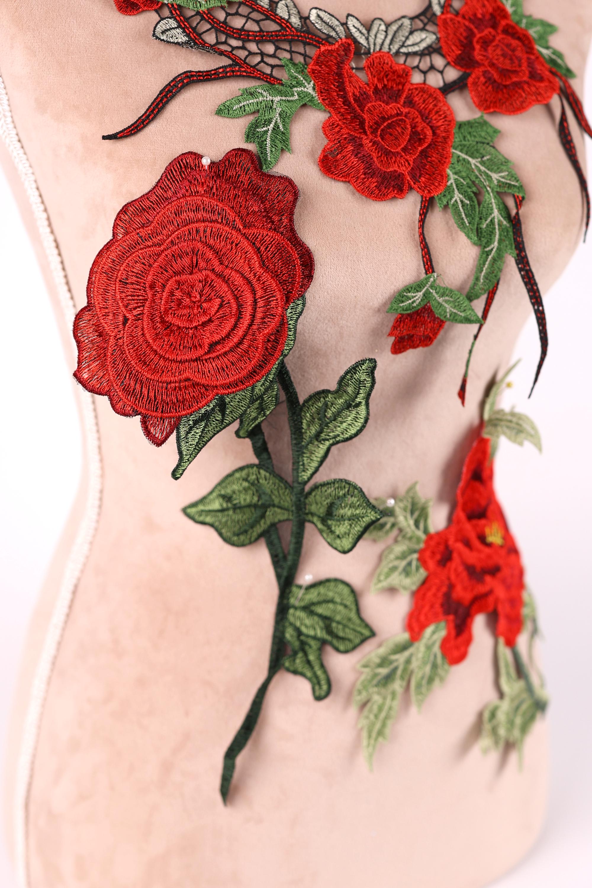 a mannequin with a beige body and red floral embroidery on its torso. The embroidery includes red roses and green leaves, creating a vibrant and eye-catching design.