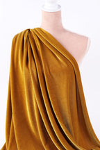 A mannequin wearing a gold velvet fabric draped over its shoulder.