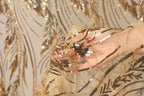 A hand is holding a piece of fabric with gold and black sequin details, against a background of gold and black sequin patterns.